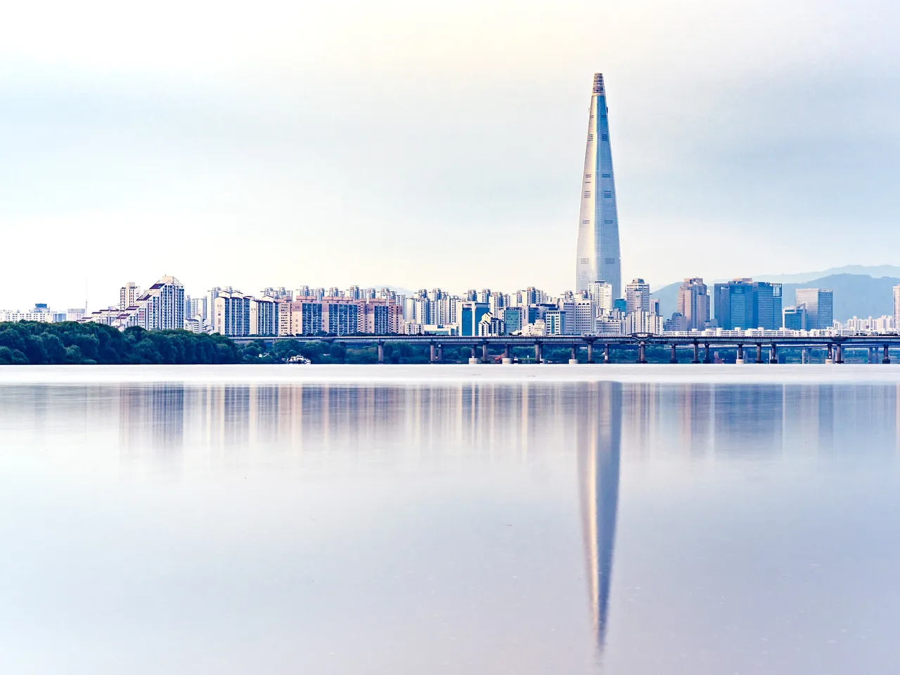 한강 너머로 보이는 서울 잠실의 롯데월드타워와 아파트 단지. 잔잔한 수면에 건물이 비친다.